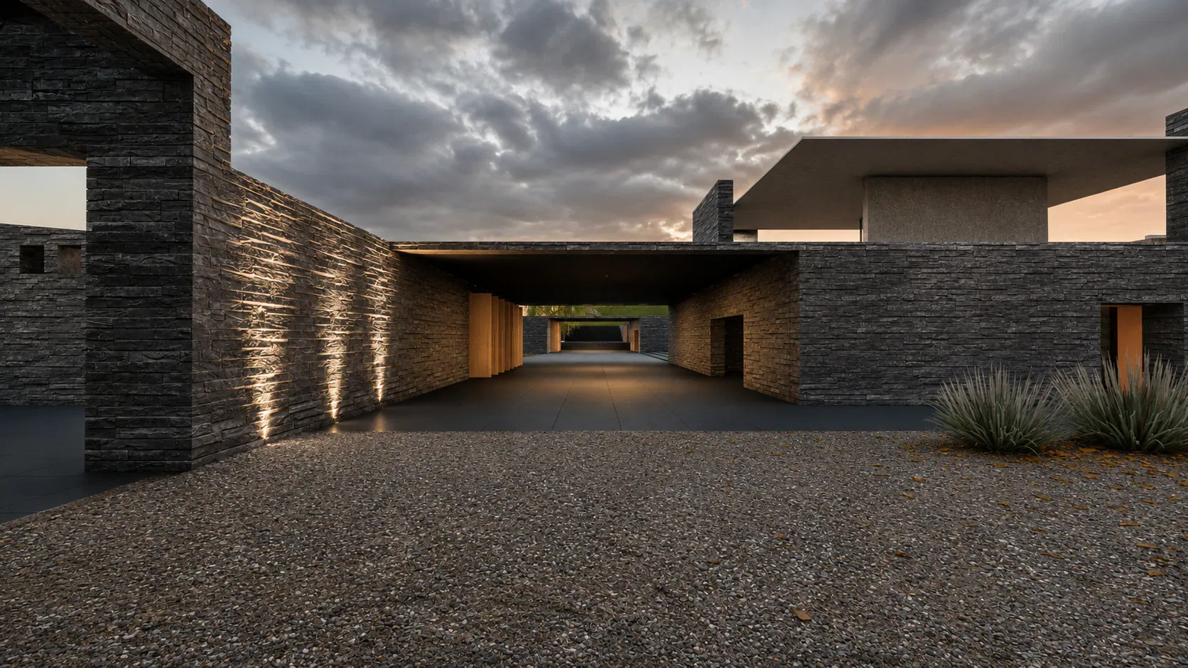 Render del acceso al centro de visitantes al atardecer: muro de piedra oscura y un pasaje central que atraviesa el volumen.
