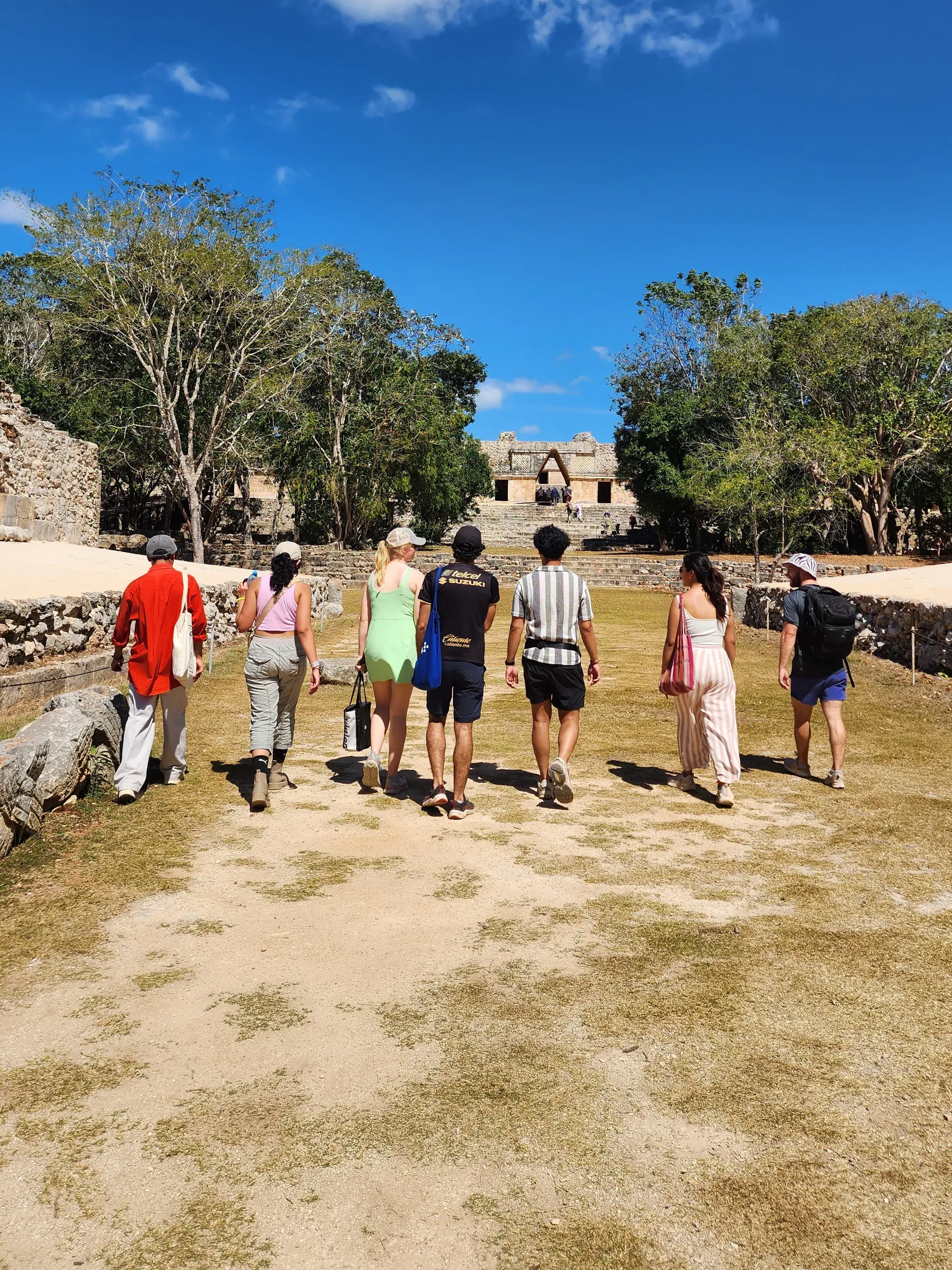 Grupo de estudiantes de la UNAM y UT Austin caminando por la zona arqueológica de Uxmal, con una estructura maya al fondo.