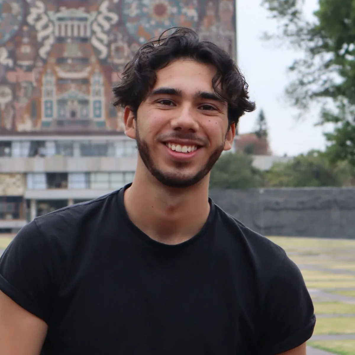 Retrato de Kaleb Shai Ortega Robinson al aire libre, con un edificio de la ciudad al fondo.
