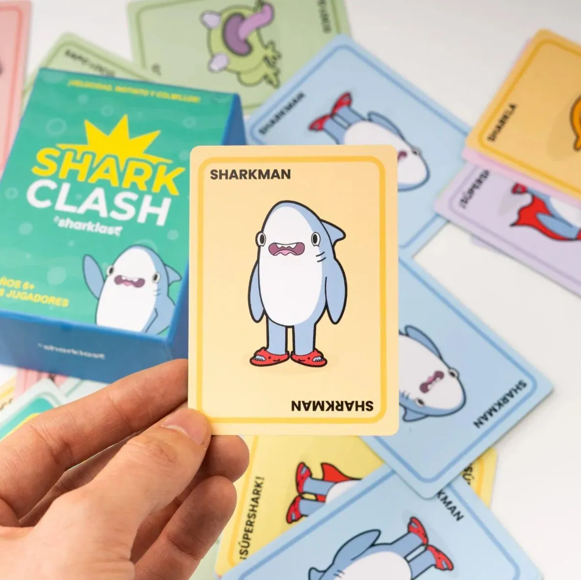 Mano sosteniendo la carta Sharkman del juego Shark Clash, con el resto del mazo de colores desplegado debajo.