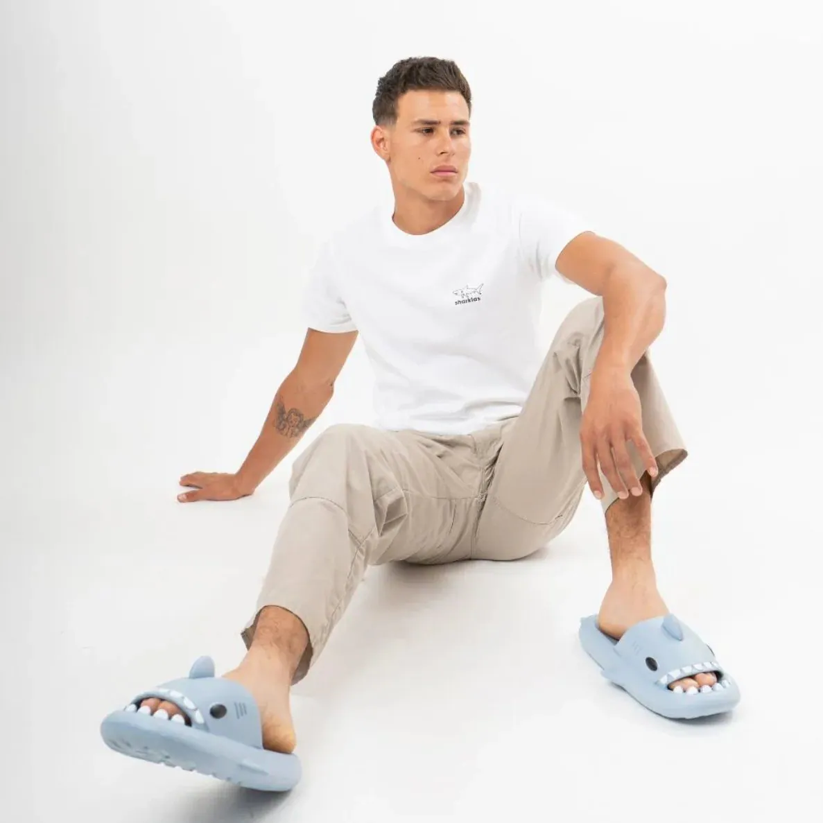 Modelo sentado con camiseta blanca de logotipo discreto y chanclas Sharklas azul claro.