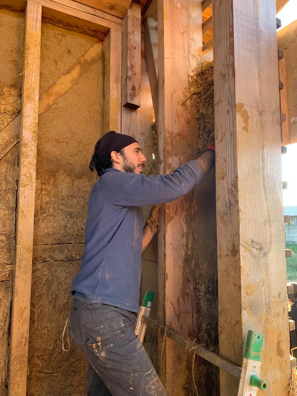 Una persona aplicando mezcla de barro sobre la estructura de madera de un muro, dentro del prototipo de casa.