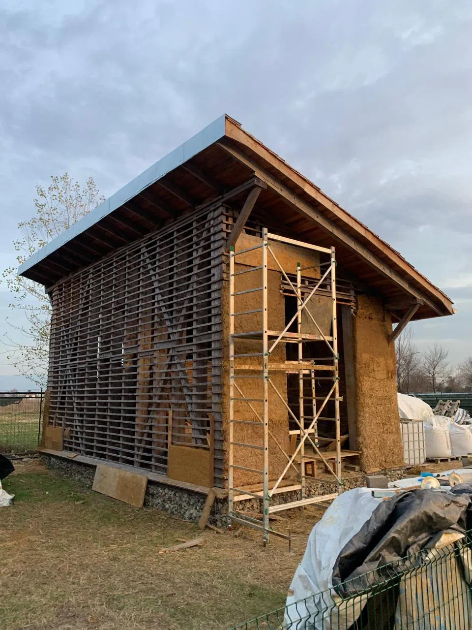 Prototipo de casa de bajo impacto terminado en su estructura: cubierta a dos aguas, muros de paja y madera, andamios alrededor.